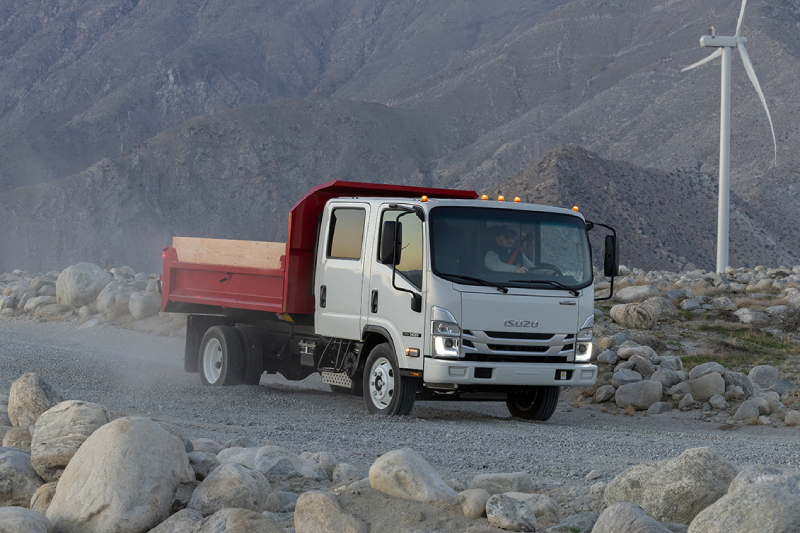 2 Isuzu trucks parked next to each other with farm land in the background.